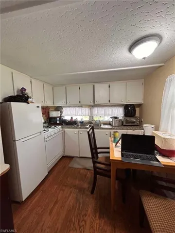Kitchen with a textured ceiling, white cabinets, dark hardwood / wood-style floors, and white appliances