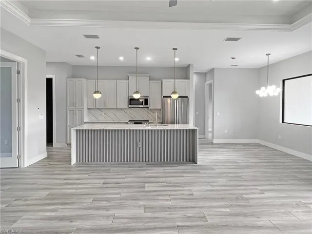 Kitchen with an island with sink, stainless steel appliances, light wood-style flooring, suspended lighting, and light stone countertops