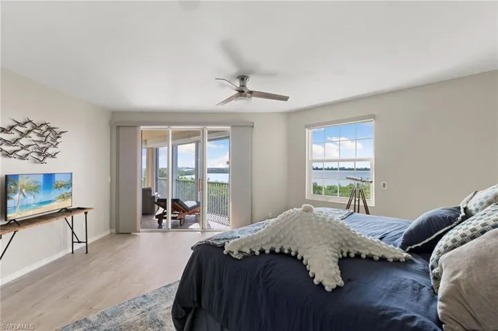 Bedroom featuring access to outside, light hardwood / wood-style flooring, ceiling fan, and a water view