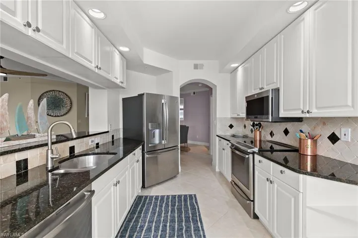 Kitchen with white cabinets, sink, light tile patterned flooring, dark stone countertops, and appliances with stainless steel finishes