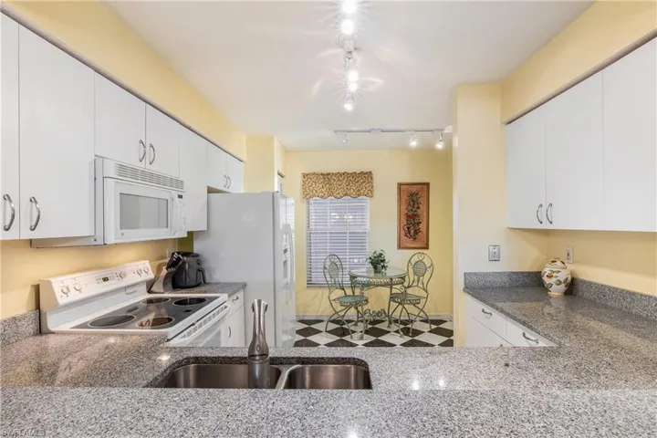 Kitchen featuring white cabinetry, dark stone countertops, white appliances, and track lighting