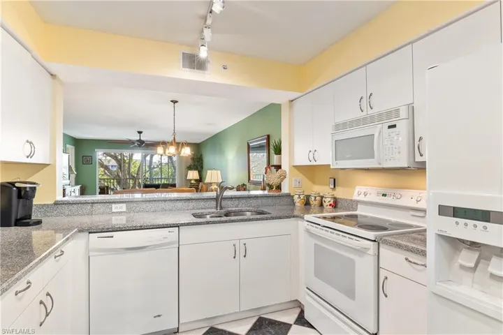 Kitchen featuring sink, track lighting, white appliances, white cabinets, and ceiling fan with notable chandelier