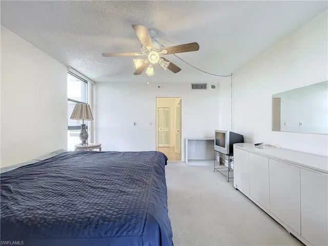 Bedroom with a textured ceiling, light colored carpet, a ceiling fan, and visible vents