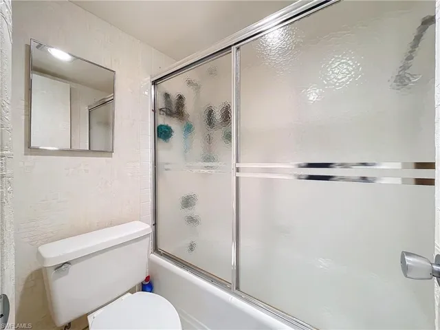 Full bathroom with toilet and combined bath / shower with glass door