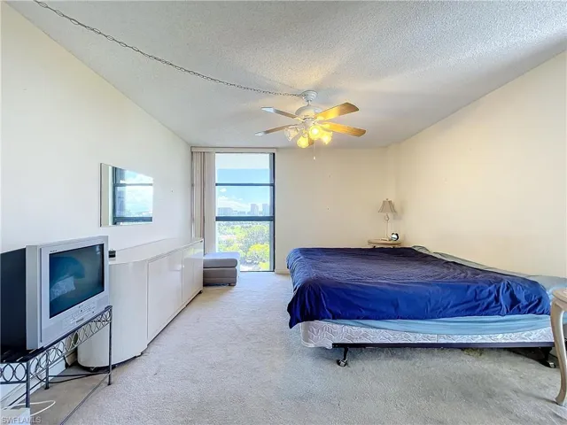 Bedroom featuring a wall of windows, ceiling fan, light carpet, and a textured ceiling