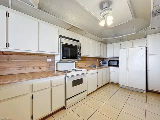 Kitchen with white appliances, light tile patterned floors, light countertops, white cabinets, and a sink