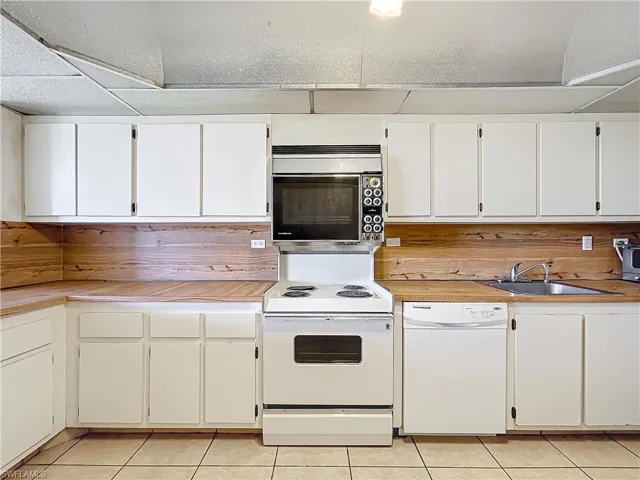 Kitchen with a sink, light tile patterned floors, light countertops, and white appliances