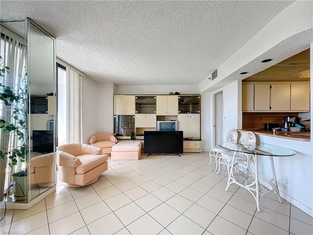Living area with a textured ceiling, light tile patterned flooring, and visible vents