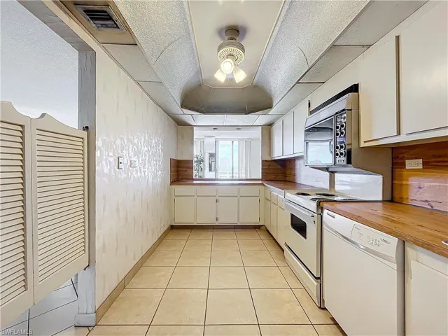 Kitchen with range, visible vents, stainless steel microwave, white dishwasher, and wooden counters