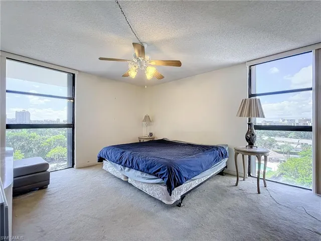Bedroom featuring a ceiling fan, a textured ceiling, multiple windows, and carpet floors
