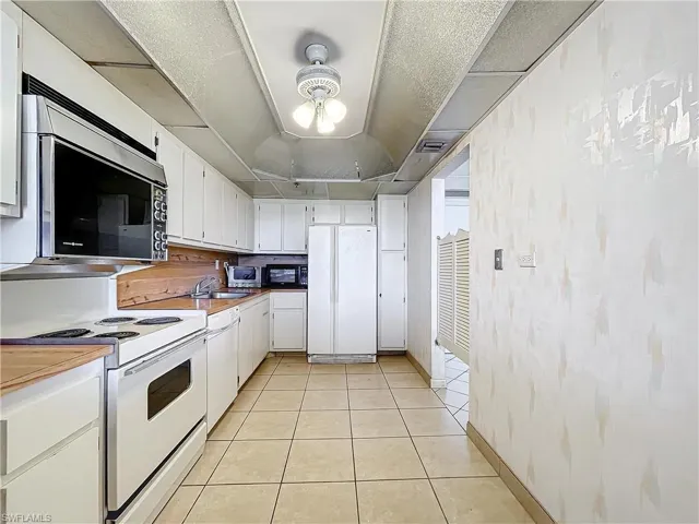 Kitchen with visible vents, white cabinets, a sink, white appliances, and light tile patterned flooring