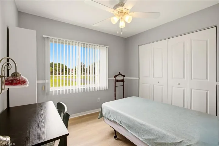 Bedroom featuring light walls with a chair rail, a large window with vertical blinds, wood-finish flooring, a ceiling fan with integrated lighting, and bi-fold closet doors