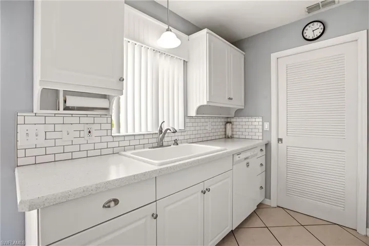 Kitchen featuring white cabinetry, light-toned countertops, subway tile backsplash, and a built-in sink with a chrome faucet