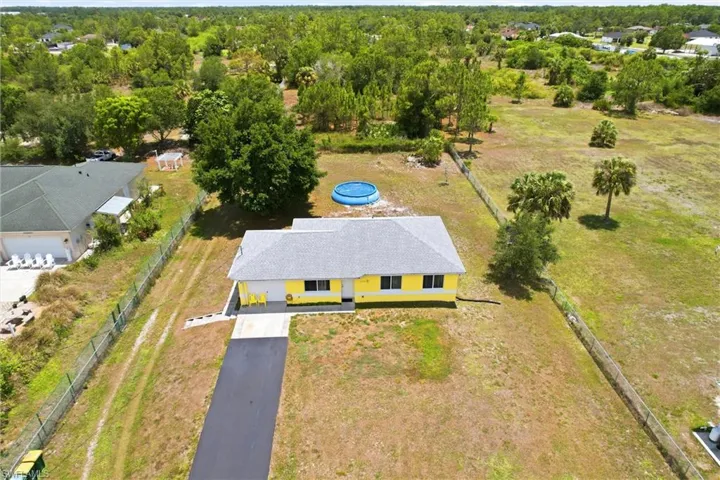 Yellow single-story residence with a gray shingle roof, dark-framed windows, and a paved driveway