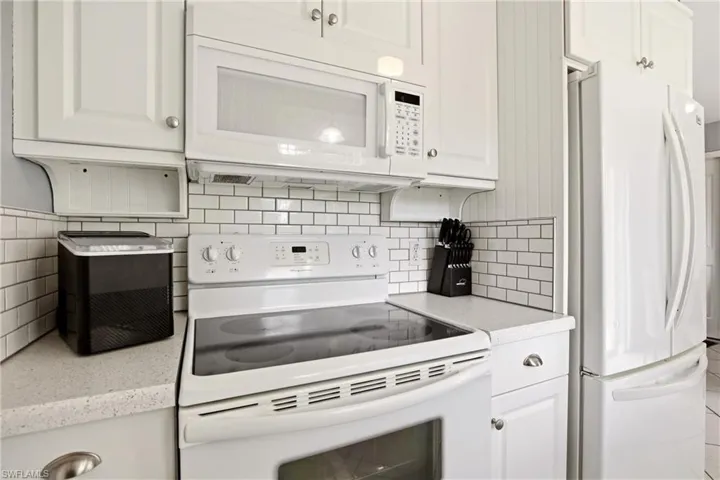 Kitchen featuring white cabinetry, subway tile backsplash, white oven range, white built-in microwave, and white refrigerator