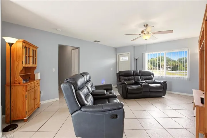 Spacious living area featuring tile flooring, a large window with vertical blinds, and a ceiling fan with integrated lighting