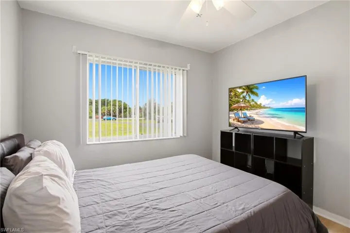 Bedroom featuring a large window with vertical blinds, light gray wall paint, and a ceiling fan with integrated lighting
