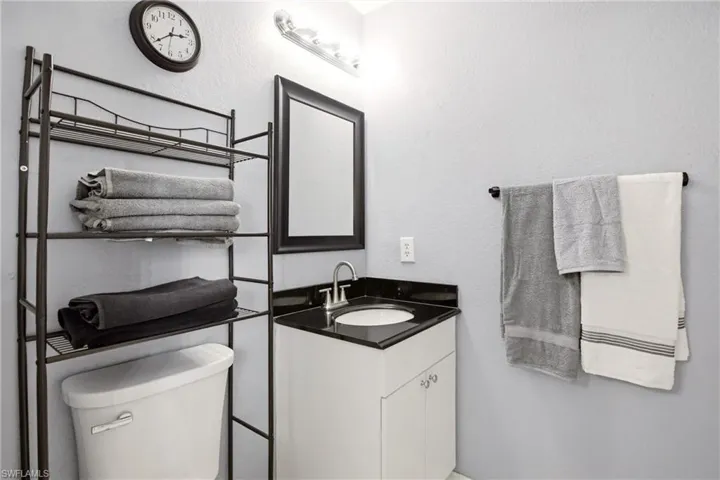 Bathroom featuring a white vanity with dark countertop, undermount sink, wall-mounted mirror with black frame, and overhead lighting fixture