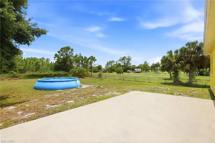 Expansive concrete patio overlooking a vast grassy area with mature palm trees and distant fencing