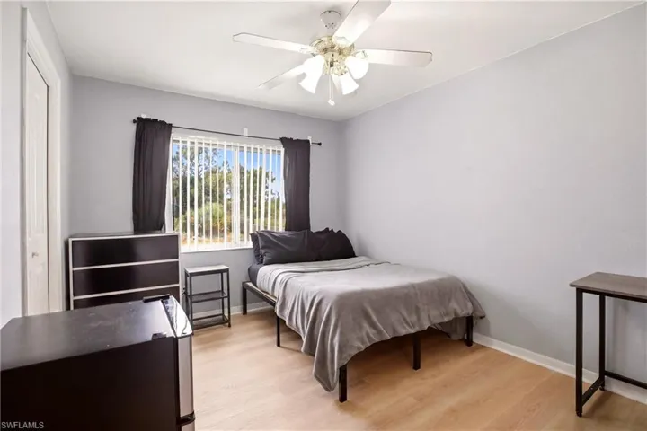 Light-filled room featuring wood-finish flooring, a ceiling fan with integrated lighting, and a window with vertical blinds