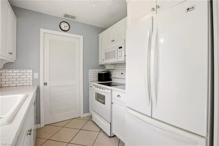 Bright kitchen featuring white cabinetry, subway tile backsplash, white appliances, and a louvered pantry door