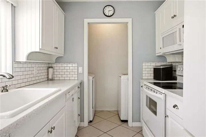 Galley-style kitchen featuring white cabinetry, subway tile backsplash, solid surface countertops, and white appliances including a built-in microwave and dishwasher