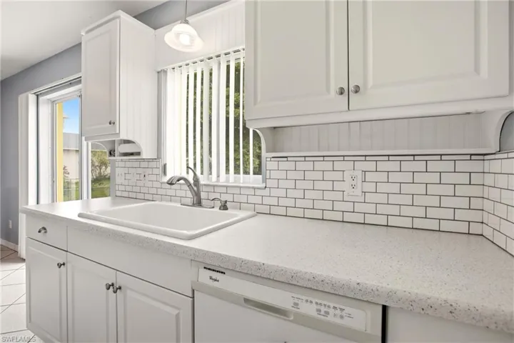 White kitchen cabinetry with brushed nickel hardware, white subway tile backsplash, and light-toned countertop