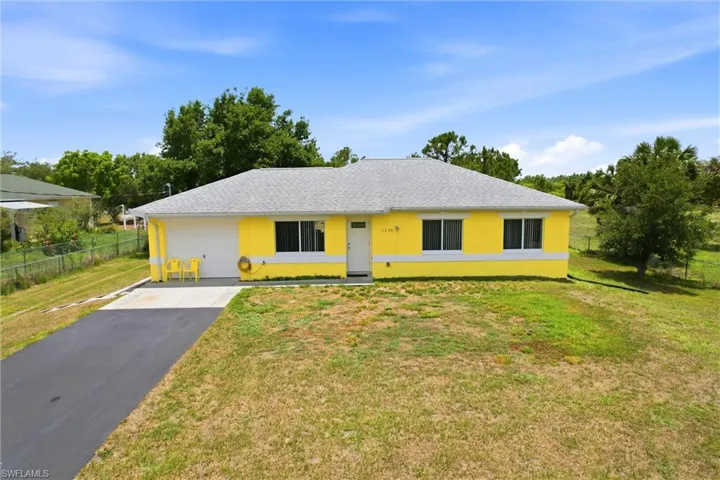 Single-story residence featuring a brightly colored exterior, a gray shingle roof, and a paved driveway leading to an attached garage