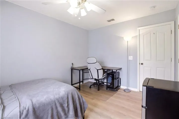 Bright room featuring light wood-finish flooring, a ceiling fan with integrated lighting, and a paneled white door