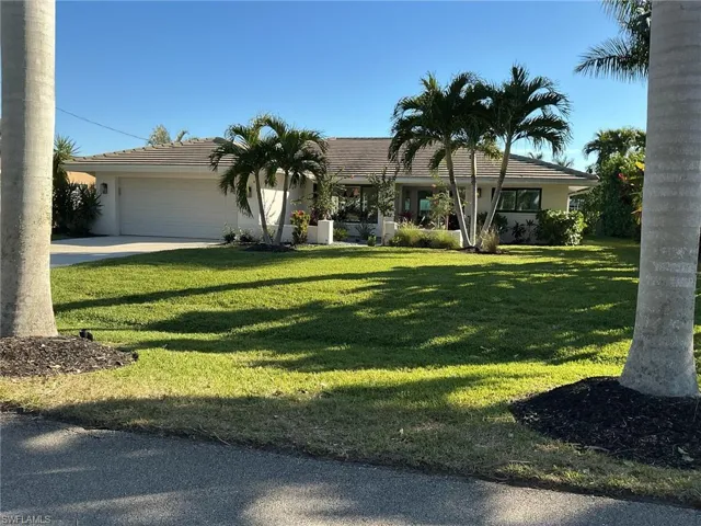 Ranch-style home with a garage, a front lawn, driveway, a tile roof, and stucco siding