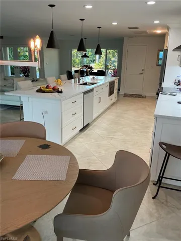 Kitchen with white cabinets, light stone counters, a breakfast bar area, a large island, and decorative light fixtures