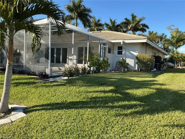 Rear view of house with glass enclosure, a sunroom, a yard, stucco siding, and a tiled roof