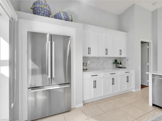 Kitchen with stainless steel appliances, white cabinetry, light stone counters, backsplash, and light tile patterned floors