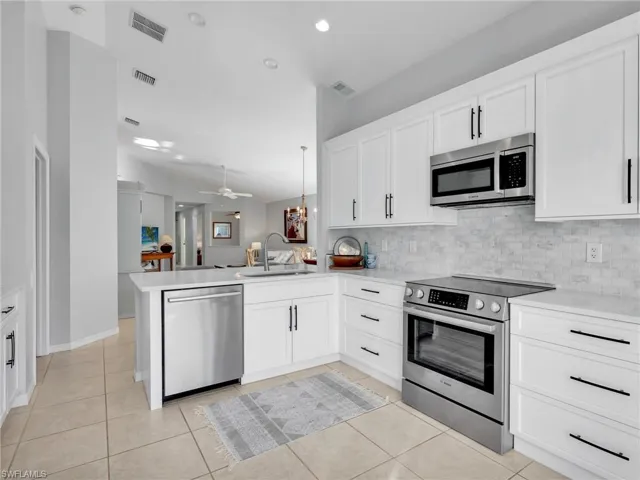 Kitchen featuring appliances with stainless steel finishes, white cabinetry, light tile patterned floors, backsplash, and lofted ceiling