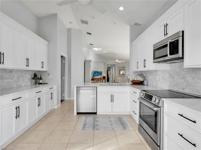 Kitchen featuring tasteful backsplash, stainless steel appliances, ceiling fan, white cabinetry, and vaulted ceiling