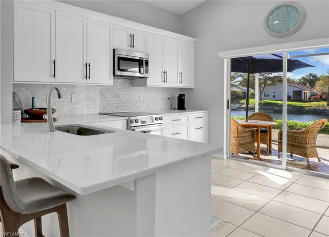 Kitchen featuring appliances with stainless steel finishes, white cabinetry, light stone countertops, light tile patterned floors, and a peninsula