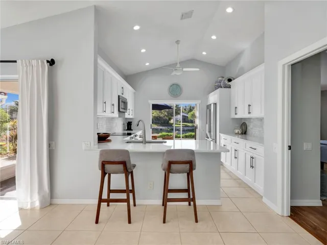 Kitchen featuring a kitchen breakfast bar, white cabinetry, a peninsula, backsplash, and light stone countertops