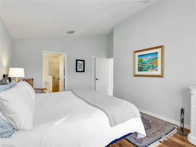 Bedroom featuring vaulted ceiling, wood finished floors, and ensuite bathroom