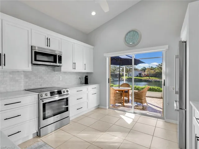 Kitchen with white cabinets, stainless steel appliances, light tile patterned floors, decorative backsplash, and a water view