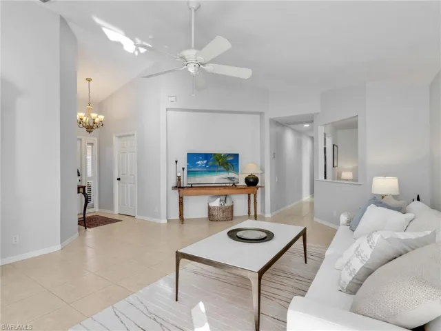 Living room with light tile patterned flooring, a ceiling fan, a chandelier, and high vaulted ceiling