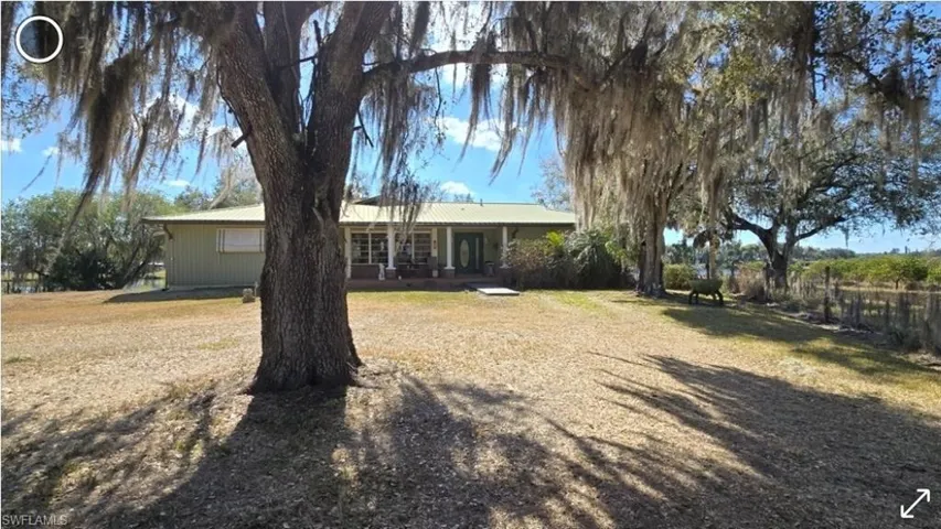 Front of home with a metal roof, covered porch, and oak laden yard.