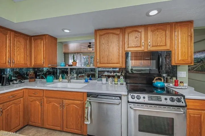 Kitchen featuring stainless steel appliances, wood cabinetry, Corian Countertops, a ceiling fan, and recessed lighting