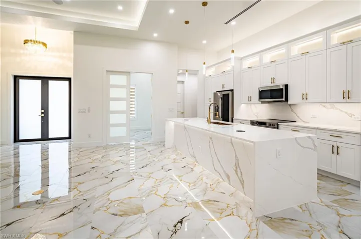 Kitchen featuring a waterfall island, integrated sink, stainless steel appliances, and white cabinetry