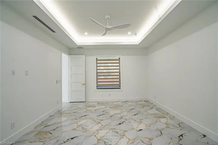Recessed ceiling with integrated lighting, modern ceiling fan, large window with horizontal blinds, five-panel interior door, and large-format tile flooring