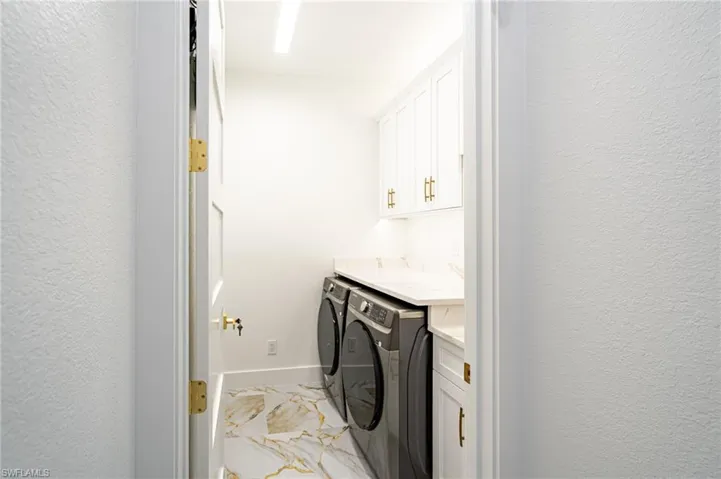 White cabinetry with gold-tone hardware, undermount lighting, and a light-toned countertop