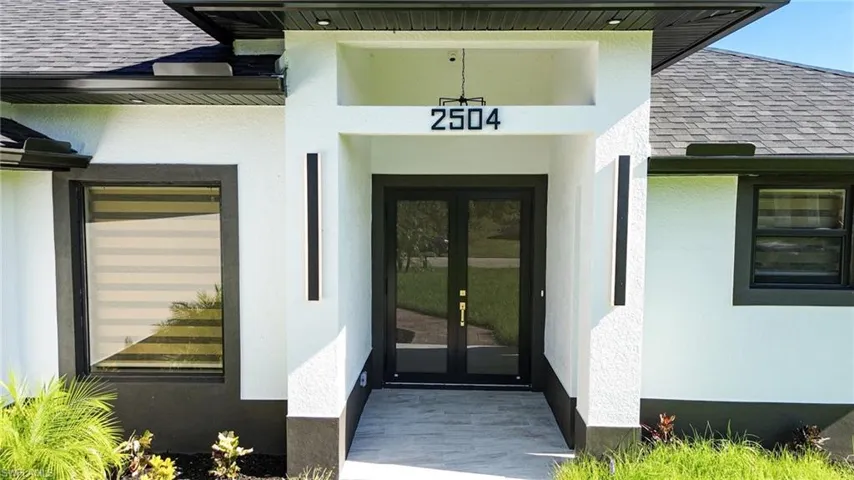 Modern exterior with a contrasting dark roof and fascia, stucco finish, dual entry doors, and flanking vertical light fixtures