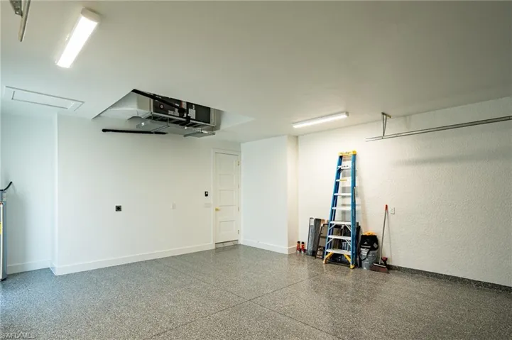 Garage featuring an epoxy coated floor, white walls, overhead lighting, and an access door