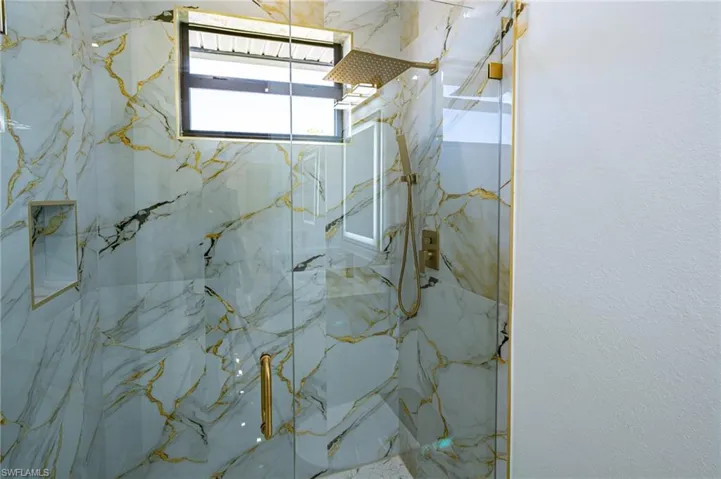 Glass-enclosed shower with gold-veined wall tile, built-in shower niche, and gold-finish shower fixtures