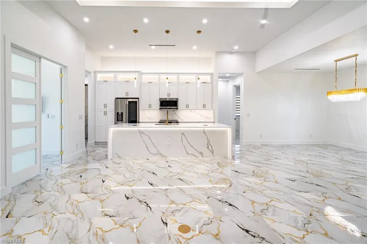 Open-concept living space with large format porcelain tile flooring, a kitchen featuring an expansive center island with under-cabinet lighting, high ceilings, and recessed lighting