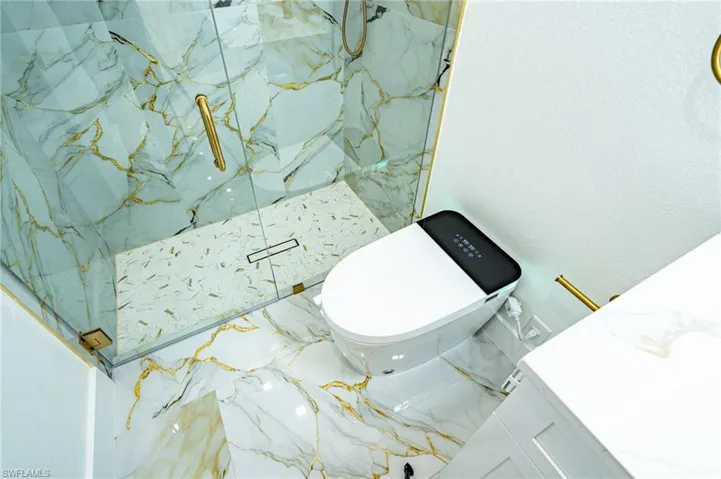 Glass-enclosed shower with gold-accented marble-style wall and floor tiling